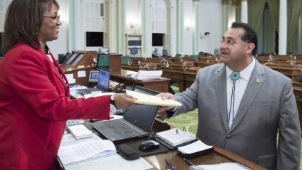 Assemblymember Ramos handing bill across the desk