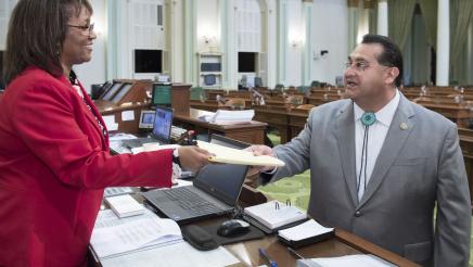 Assemblymember Ramos handing bill across the desk