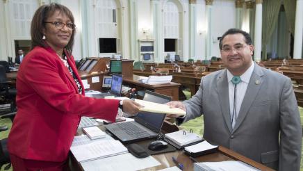 Assemblymember Ramos handing bill across the desk